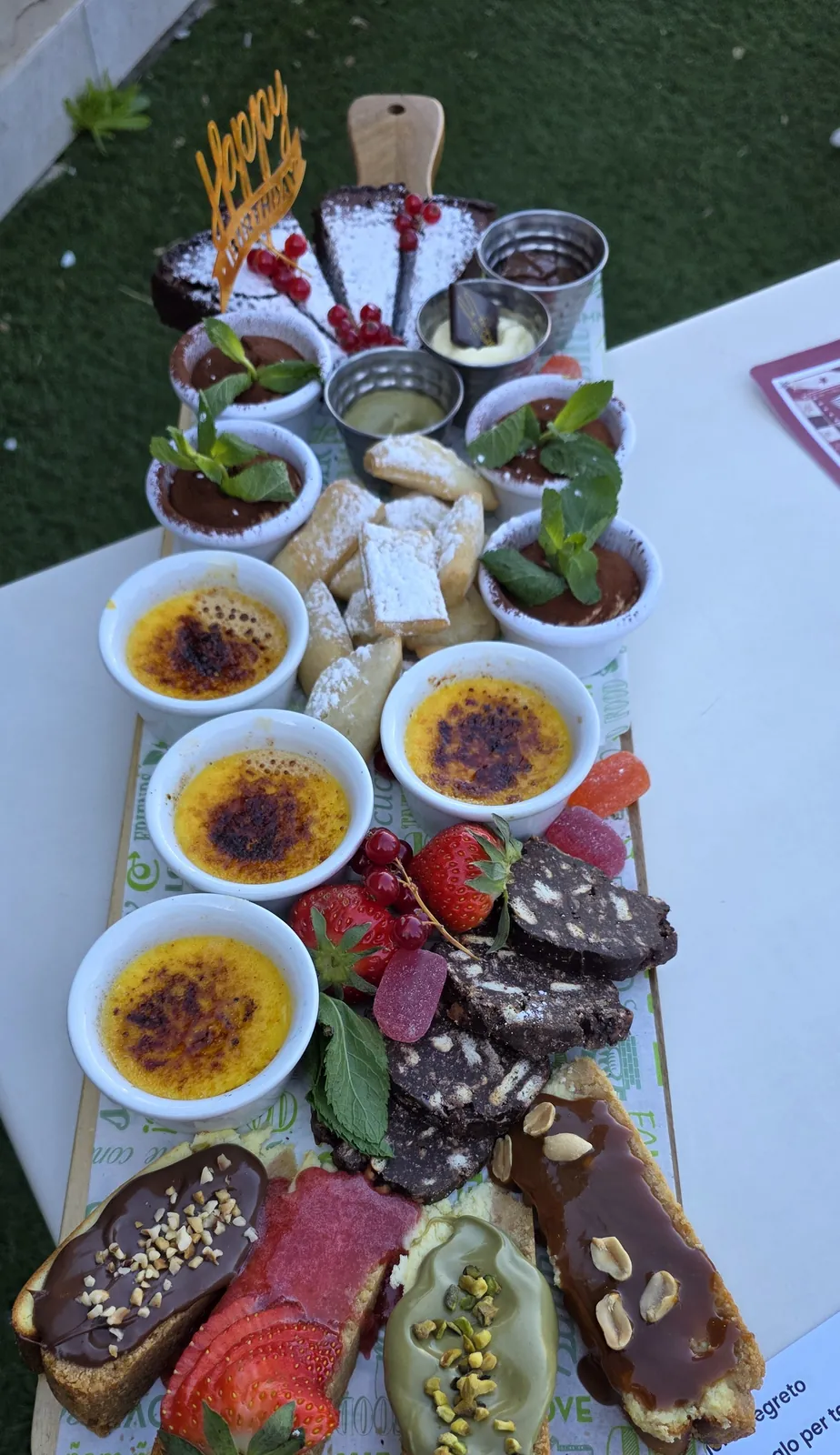 Tagliere della degustazione di dolci con crème brûlée, salame di cioccolato e pasticcini su un tavolo in giardino