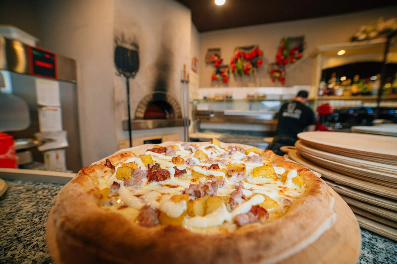 Pizza appena sfornata sul tagliere, con il forno a legna e la sala della Brasserie alle spalle