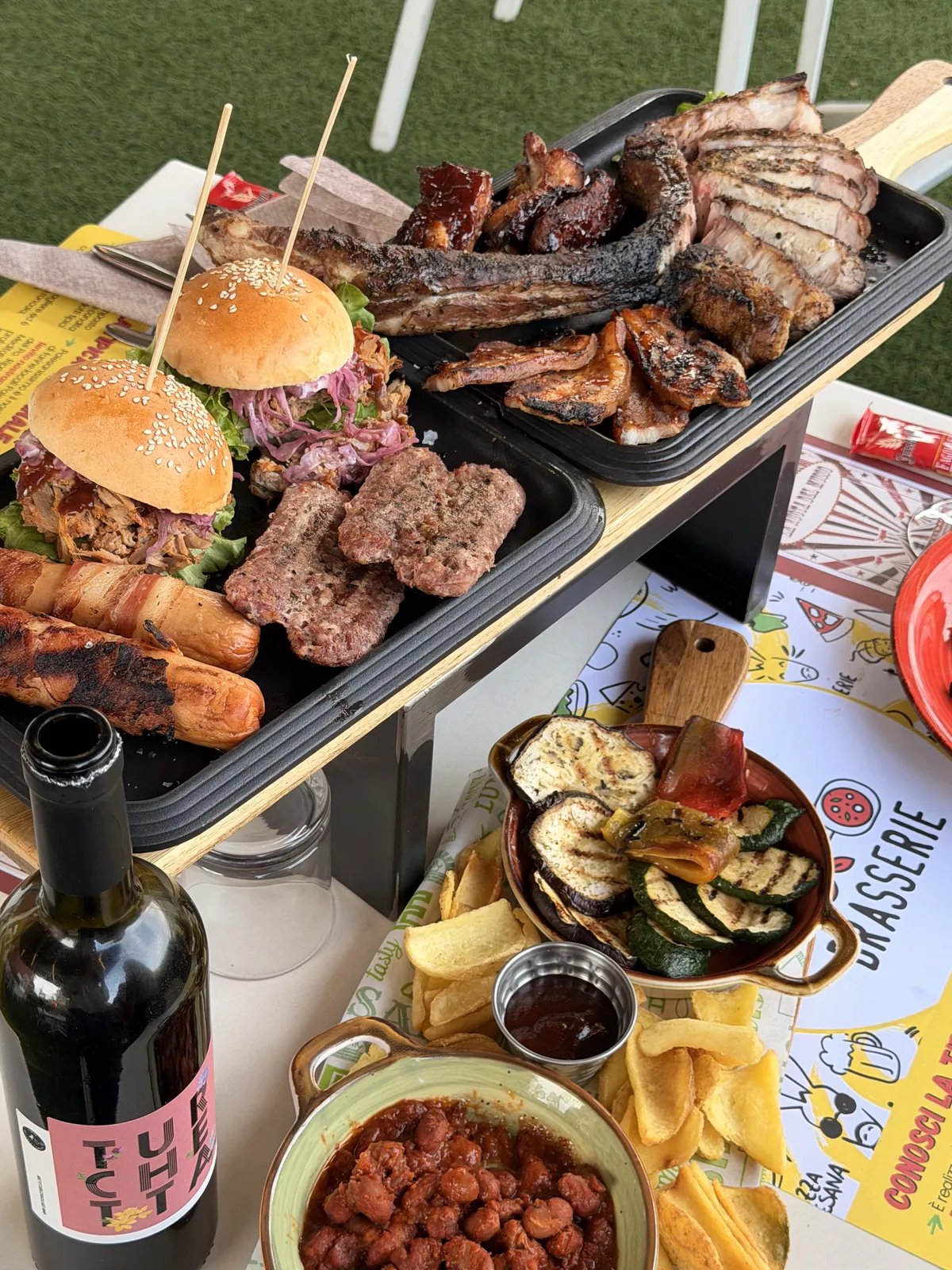 Grigliata con costate, salsicce, burger e verdure sul tavolo in giardino con la tovaglietta della Brasserie