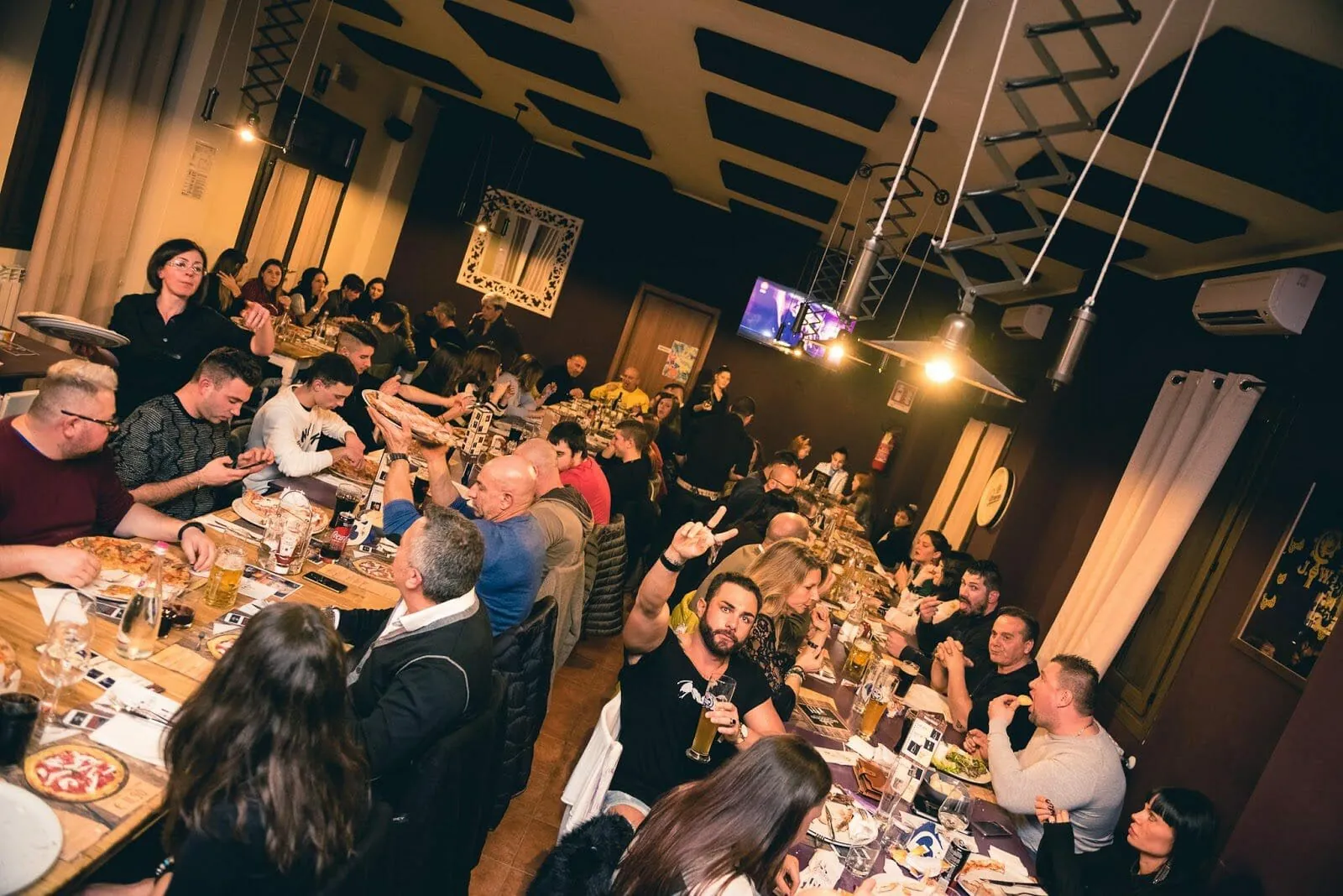 La sala della Brasserie piena di gente seduta alle tavolate, fra luci calde e boccali di birra