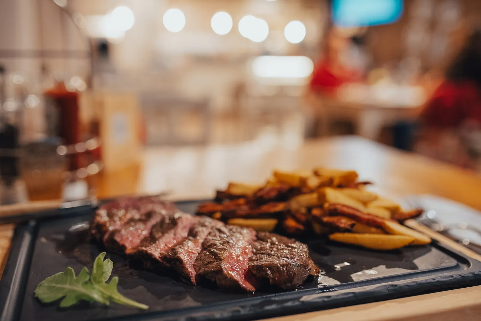 Tagliata di manzo con patatine sulla piastra di ghisa, con la sala della Brasserie illuminata dietro