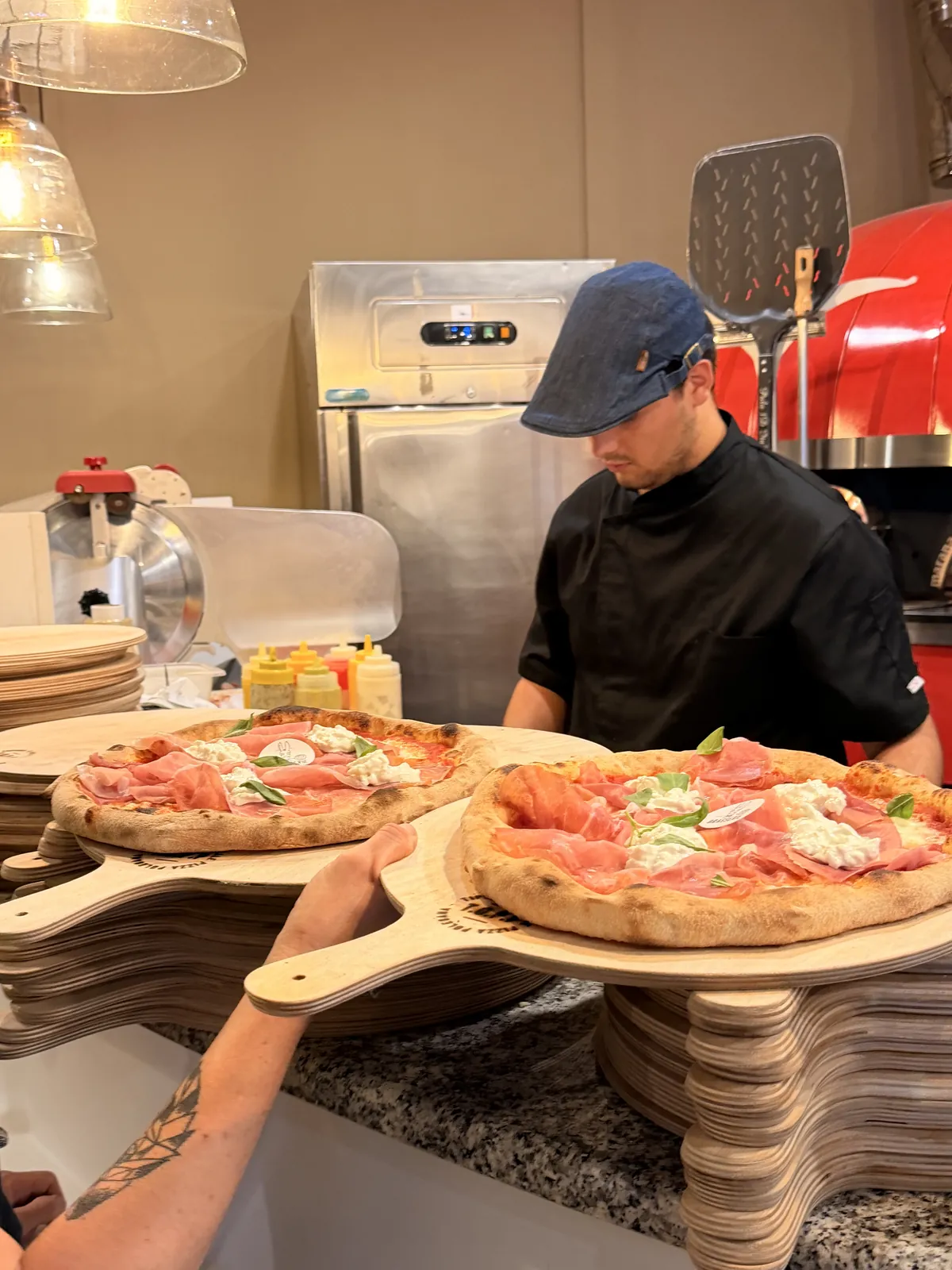 Il pizzaiolo serve due pizze sui taglieri davanti al forno della Brasserie